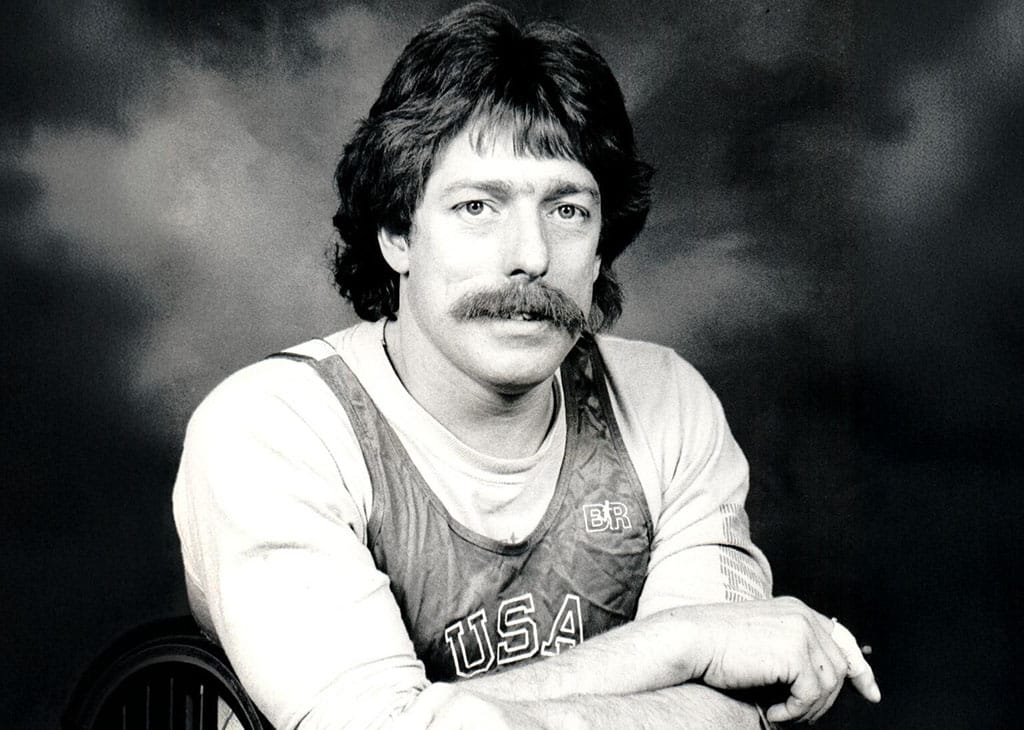Black-and-white portrait of Bob Hall wearing a USA athletic singlet, seated and looking directly at the camera.